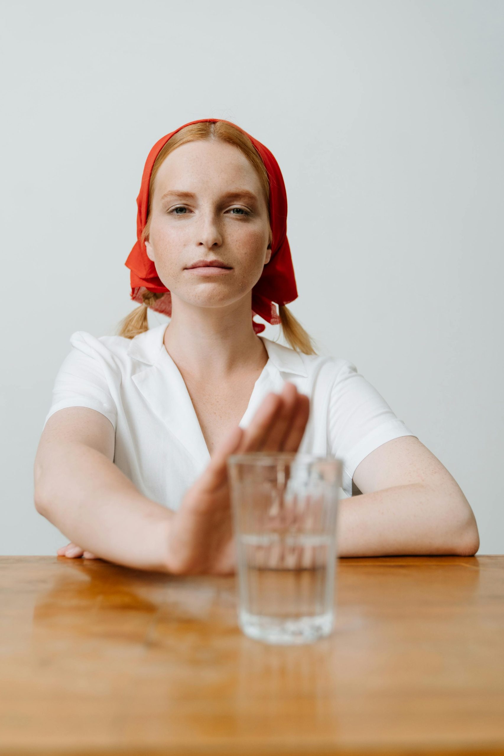Caucasian woman with red kerchief refusing a vodka drink, symbolizing sobriety.